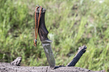 hunting knife with metall skull bead on leather lace stuck in a wooden log