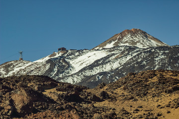 Mountain Teide with white snow spots, partly covered by the clouds. Bright blue sky. Teide National Park, Tenerife, Canary Islands, Spain.