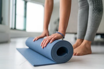Deurstickers Yogaschool Yoga thuis vrouw rollende oefenmat in de woonkamer van huis of appartement condo voor ochtend wellness yoga praktijk.