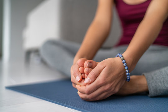 Yoga leg stretches woman at home. Seated butterfly legs stretch holding soles of feet together. Closeup of hands holding barefoot feet on exercise mat.