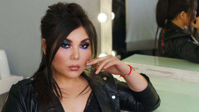 Portrait of beautiful dark haired pan-asian model with perfect make up and stylish hairdo fishbone braid. Plus size model posing sitting by mirror in beauty salon. Beauty industry