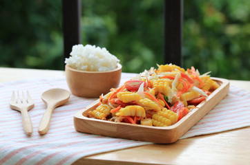 Thai traditional corn spicy salad, som tum with sticky rice in wooden plate 