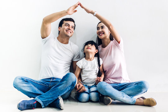 Happy family father and mother with daughter sitting and  making roof with hands arms over head on wall background