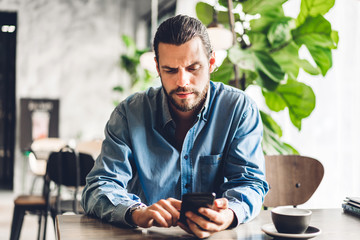 Handsome bearded hipster man use smartphone with coffee at table in cafe.Communication and...