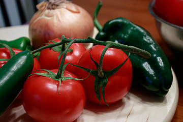 red tomatoes, green peppers, and onions scattered around on a table in a kitchen
