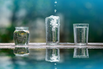 Drink water pouring in to glass over sunlight and natural green background.Water splash in glass Select focus blurred background.