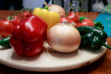red tomatoes, green peppers, and onions scattered around on a table in a kitchen