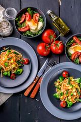 Spaghetti with vegetables and salad with arugula and mozzarella on a dark wooden background. Top view.