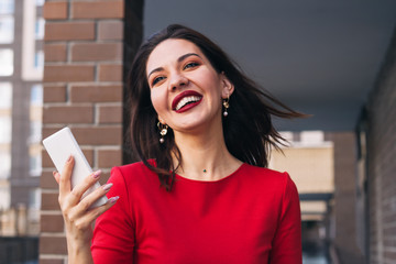 young beautiful excited happy woman with red lipstick and wearing red dress holding mobile phone...