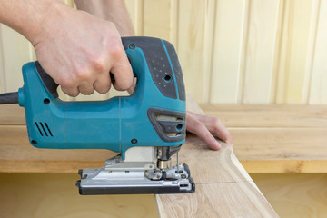 .A man is sawing a board with an electric jigsaw. A joiner's workshop. Copy space.
