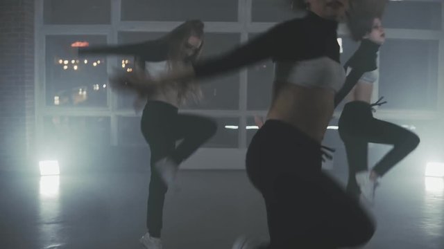 Group of young hip-hop dancers performing on the stage. Happy dancing women. Girls enjoying funky hip hop moves in dark studio with smoke and lighting