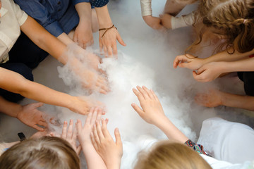 Chemical show at the birthday party: children's hands touch the smoke from liquid nitrogen. The...