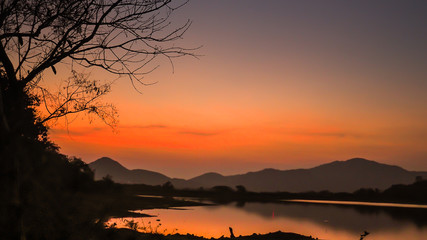 Landscape with orange and purple at sunset  silhouettes of mountains, hills and forest lake