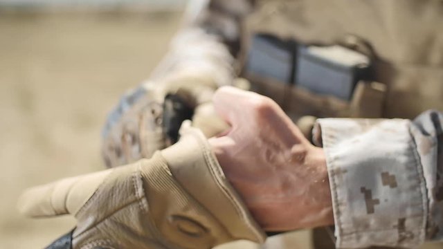 SLOW MOTION: A US Marine positioned in the desert puts a tactical glove on his left hand. Close up.