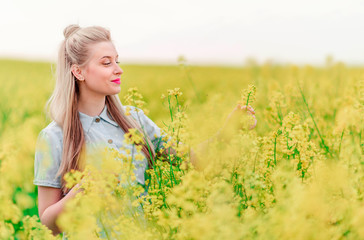 Naklejka na ściany i meble beautiful blonde girl poses for the camera in rapeseed field