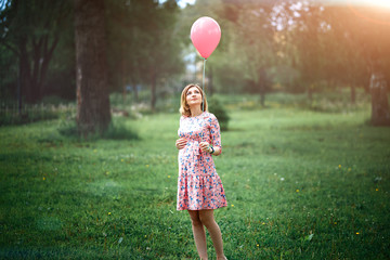 Young happy pregnant woman with pink balloon outdoors