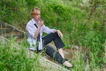 A beautiful and stylish woman with a slightly androgynous appearance with short blond hair (haircut), in a men's white shirt, black pants and tie, sits on the steps and lights a cigarette to smoke