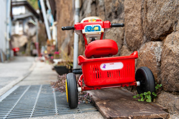 坂のある町に置いてある赤い三輪車