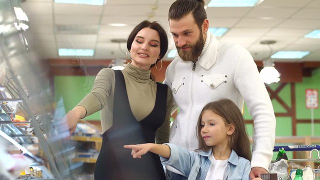 Portrait of happy family choosing bread and sweets in bakery section in supermarket. Beautiful parents and their daughter are choosing sweets and smiling while doing shopping in supermarket. Slow mo.