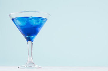 Summer cold blue lagoon drink with ice cubes in elegant martini glass on pastel mint background.