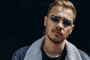 Portrait of young man in blue jeans jacket with sunglasses outdoor on dark background.