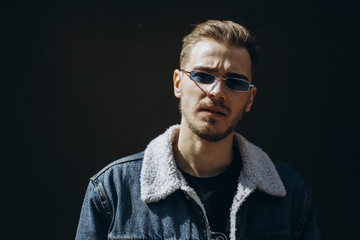 Portrait of young man in blue jeans jacket with sunglasses outdoor on dark background.