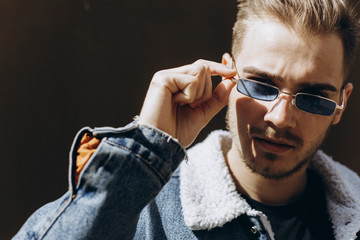 Portrait of young man in blue jeans jacket with sunglasses outdoor on dark background.