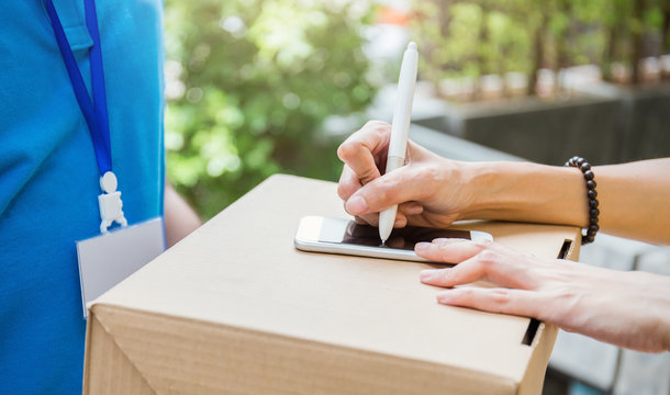 Close up woman hand appending receive sign signature after accepting a delivery of box from delivery man. Transportation shipping deliver package e-commerce telemarketing concept