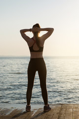 Fototapeta na wymiar girl athlete, faces the sea, looks at the dawn, goes in for sports, concept