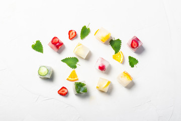 Ice cubes with fruit and mint leaves on a white stone background. Fruit ice concept, quenching thirst, summer. Flat lay, top view