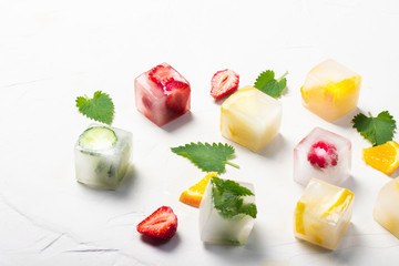 Ice cubes with fruit and mint leaves on a white stone background. Fruit ice concept, quenching thirst, summer