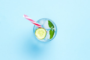 Glass of cold and refreshing water with ice, mint and cucumber on a blue background. Ice Cube. Concept of hot summer, alcohol, cooling drink, thirst quenching, bar. Flat lay, top view