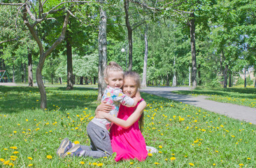 Two sisters hug each other in the park on the lawn on a warm sunny day