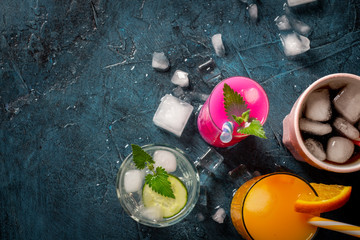 Four kinds of refreshing drinks with ice on a dark blue background and ice cubes. Concept night club, night life, party, thirst. Orange, mint and cucumber, strawberry, cola. Flat lay, top view