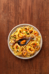 Seafood pasta. An overhead photo of a plate of tagliolini with mussels, shrimps, clams and squid rings, on a dark rustic wooden background with copyspace