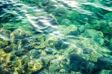 Fototapeta premium Transparent turquoise sea surface with sun glare, background. Close-up. Space for text.