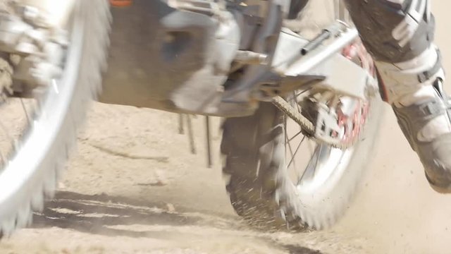 SLOW MOTION: A dirt biker rides his CRF Honda through the desert and whips around a berm. Close up of the boots around the corner and drags foot in sand and dirt.