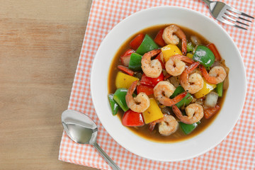 top view of stir fried shrimp with black and sweet pepper in a ceramic plate on wooden table. homemade style food concept.