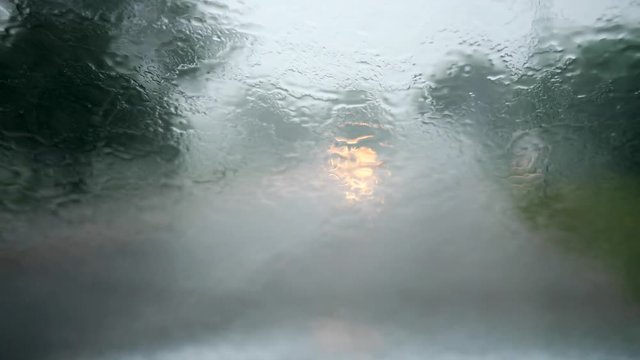 Blurred abstract view of a windshield of a car. Sitting inside the car during heavy raining. Wipers operating while cars coming and going in a traffic outside. UHD