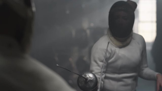 Over the shoulder of a male fencer training with a female fencer that parrys a strike in slow motion