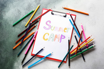 Sheet of paper with text SUMMER CAMP and pencils on color background