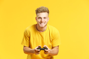 Portrait of handsome young man playing video games on color background