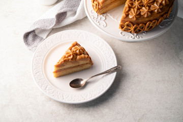 a slice of a caramel cake on a white rustic plate, on a marble backdrop