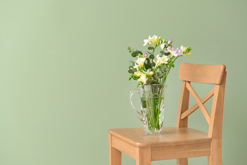 Vase with beautiful freesia flowers on chair against color background