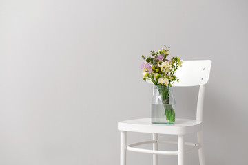Vase with beautiful freesia flowers on chair against light background
