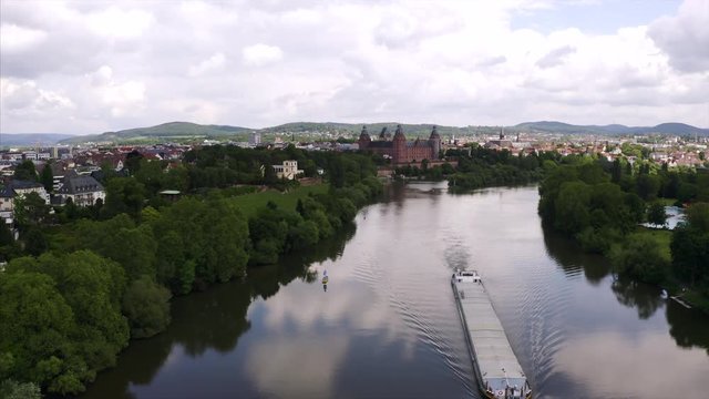 Fyling over the river Main to the Castle Johannisberg in Aschaffenburg in Bavaria. The weather is cloudy and a cargo ship is driving on the water.
