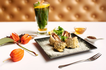 Delicious dessert on black plate decorated with physalis prepared for client. Sweet sushi roll cooking in oil with chocolate sauce and icing sugar doing by special recipe. Tasting best with mint tea.