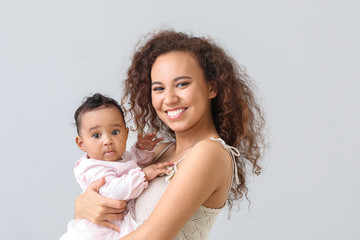 African-American woman with cute little baby on light background