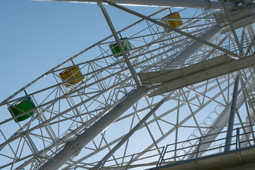 Fototapeta premium Ferris wheel with yellow and green booths against a blue sky