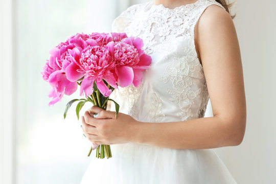 Young bride with bouquet of beautiful peonies indoors